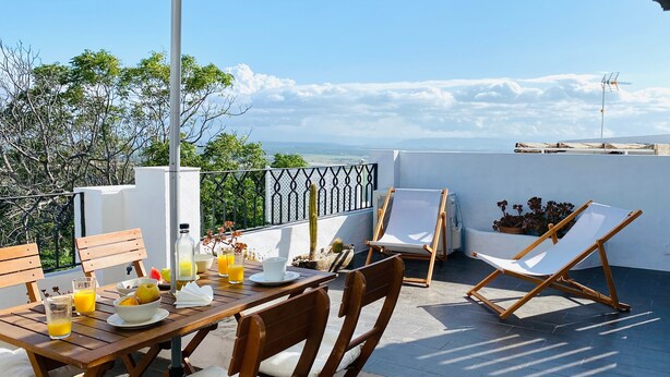 Una terraza con una mesa lista para el desayuno, una silla y vista al mar.