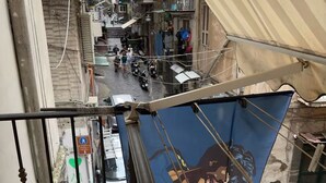 A narrow street with buildings on both sides, a blue banner with a person, and a pedestrian sign. - Residence El Diez (Naples)