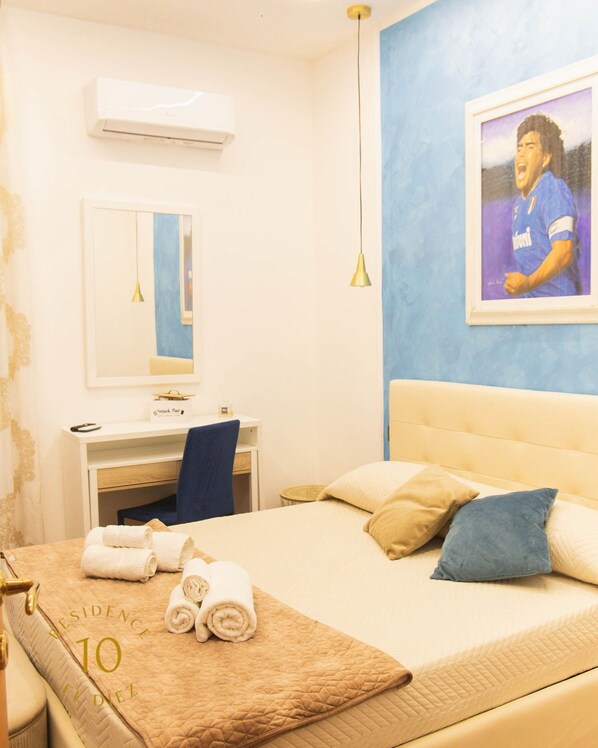 A hotel room with a bed, a desk, a chair, a mirror, and a wall-mounted air conditioner.