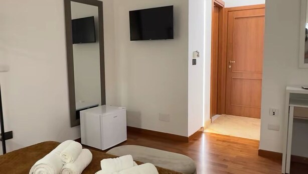 A hotel room with a bed, a large mirror, a television, and a wooden door. - Residence El Diez (Naples)