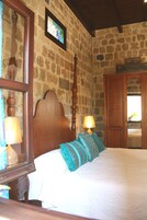 A bedroom with a stone wall, wooden headboard, and a bed with blue striped pillows.