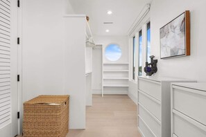 Un pasillo con una puerta blanca, una cesta de mimbre, un ventanal circular y un cuadro en la pared.