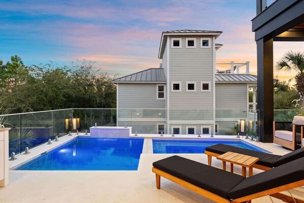 A modern pool area with lounge chairs, a clear view of a two-story building, and a glass railing.