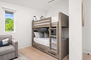 Una cama litera con escritorio y cajones, un sofá, y una ventana con vistas a zonas verdes.