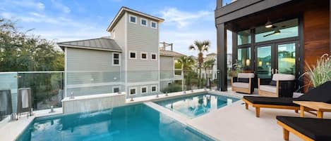 A modern pool area with a clear blue pool, lounge chairs, and a two-story building with large windows.