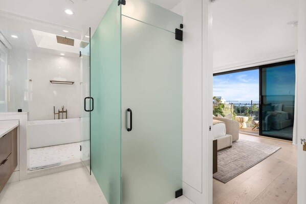 Un baño moderno con mampara de ducha de vidrio, una bañera y puerta de vidrio que da a un balcón con vistas.