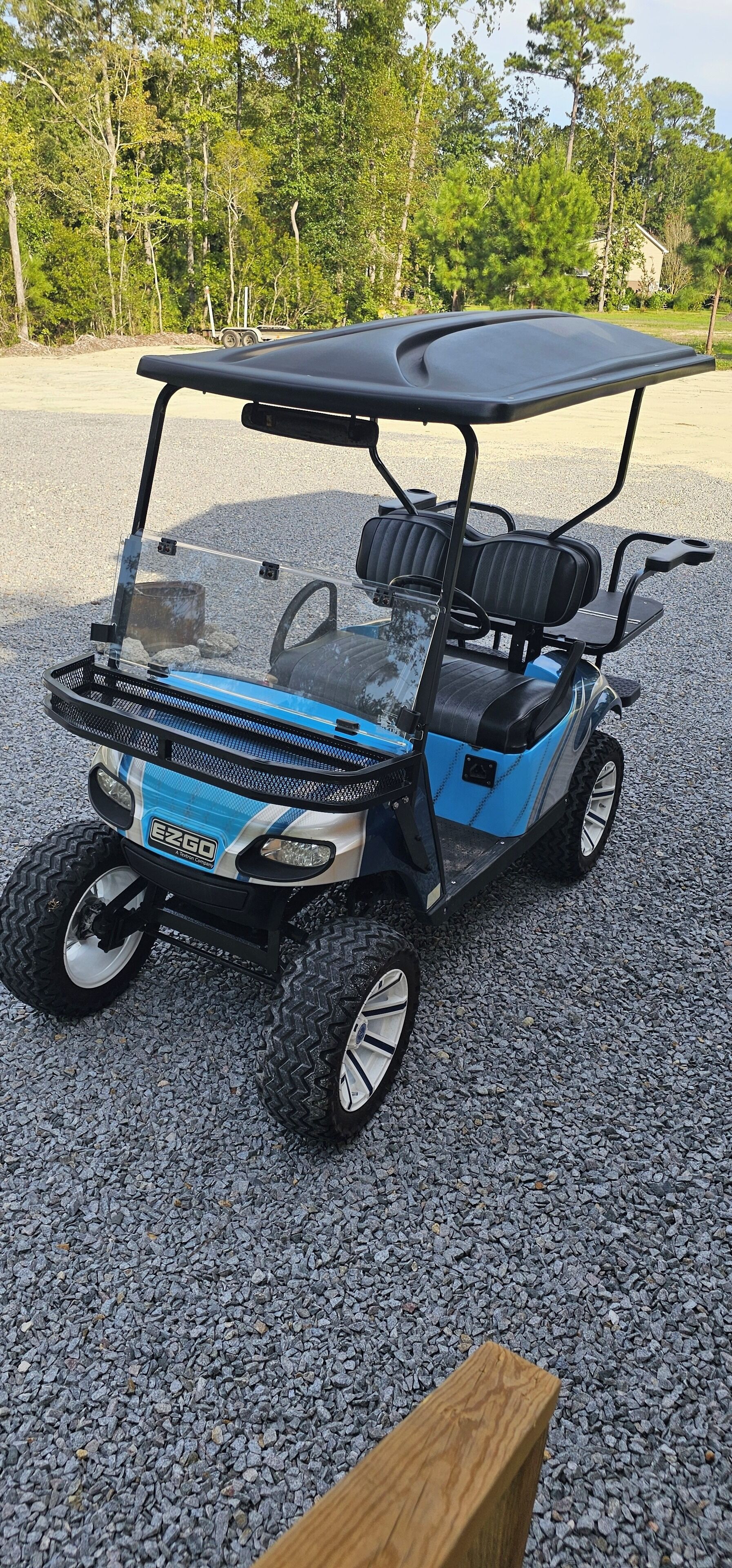A blue and black golf cart with a canopy, parked on gravel.
