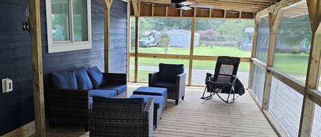 A covered outdoor seating area with wooden flooring, a ceiling fan, and a view of a grassy yard.