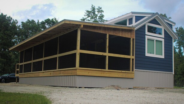 Ein zweistöckiges Haus mit einer großen, überdachten Veranda und einer kleinen angebauten Garage.