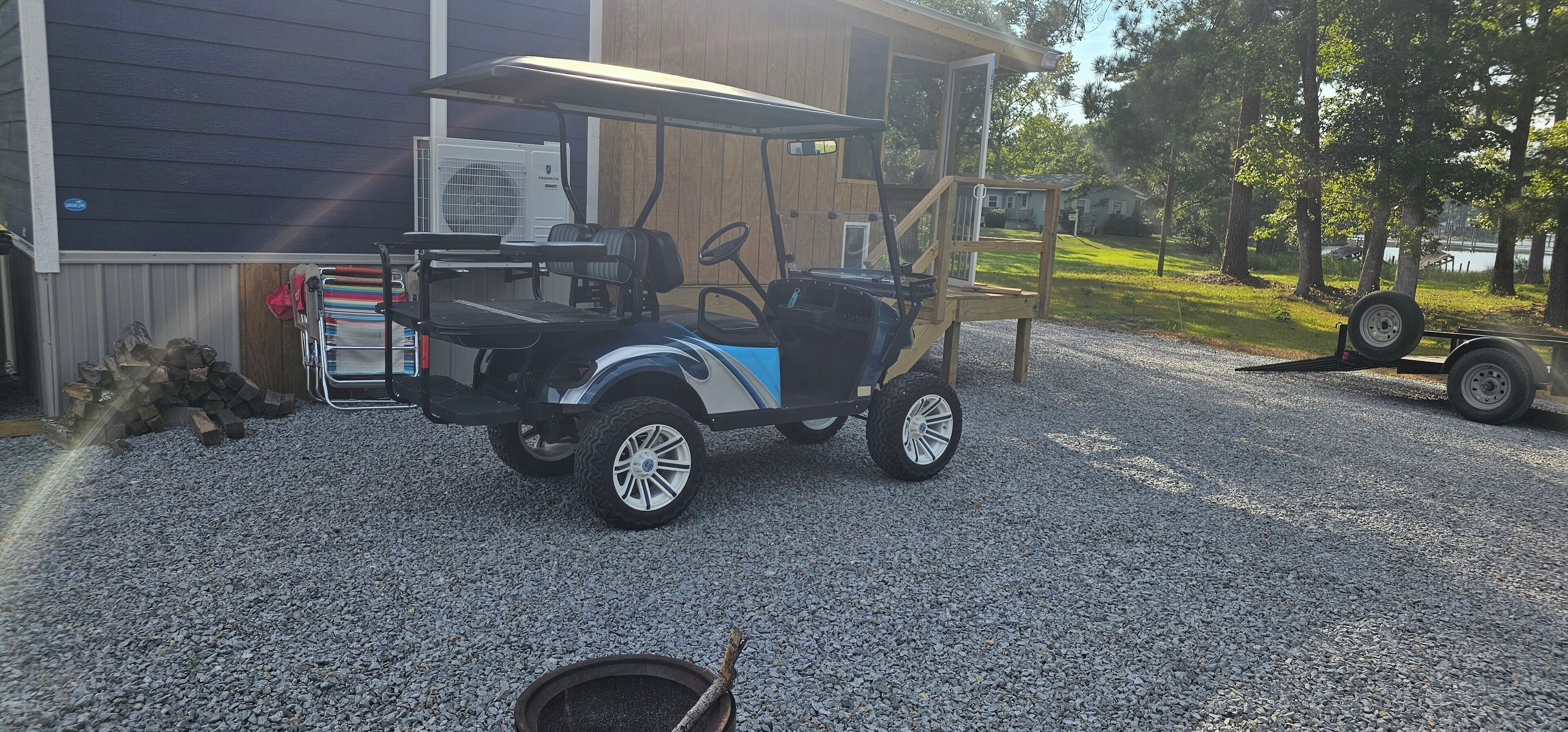A golf cart parked on gravel in front of a building with a wooden deck and a large air conditioning unit.