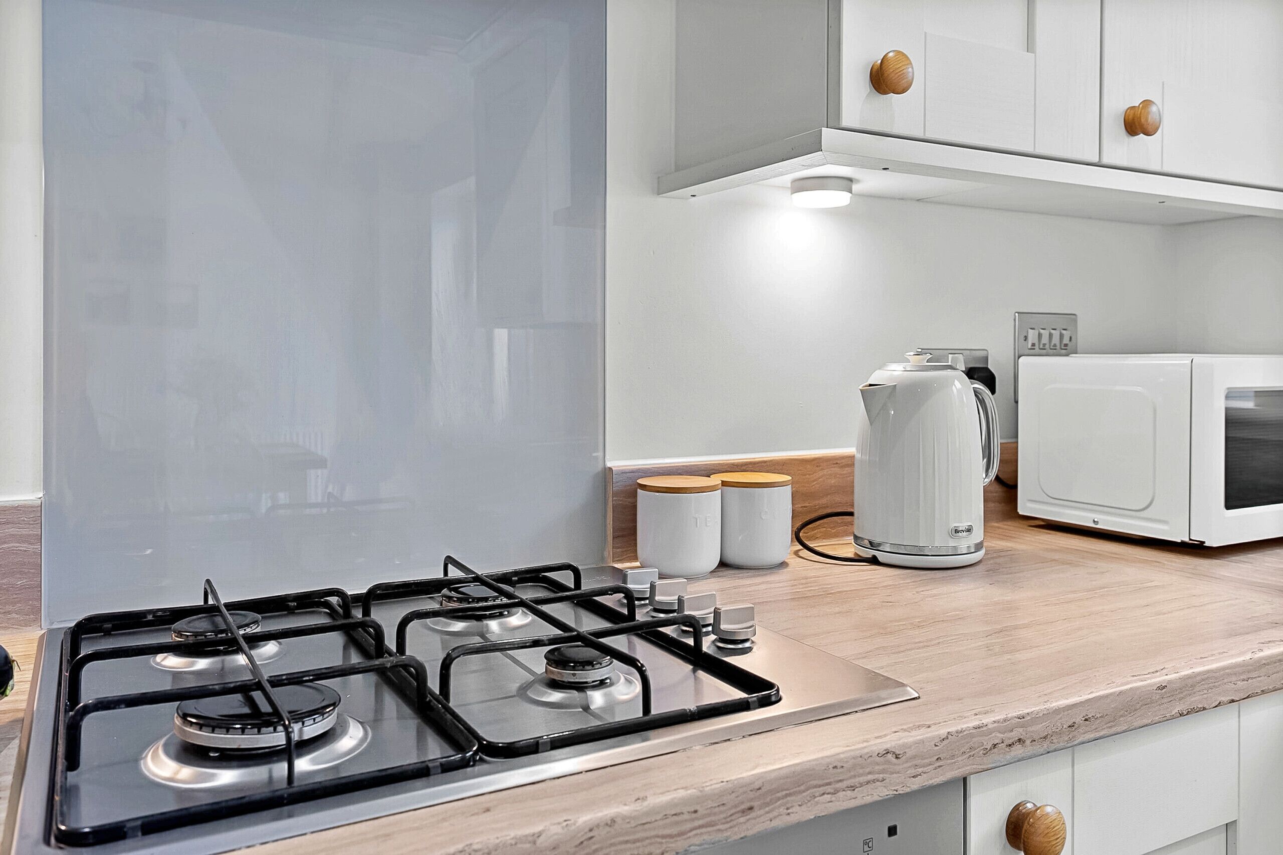 A modern kitchen with a gas stove, a microwave, and a kettle on the countertop.