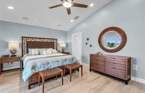 A bedroom with a bed, bedside tables, a dresser, a ceiling fan, and a large mirror.