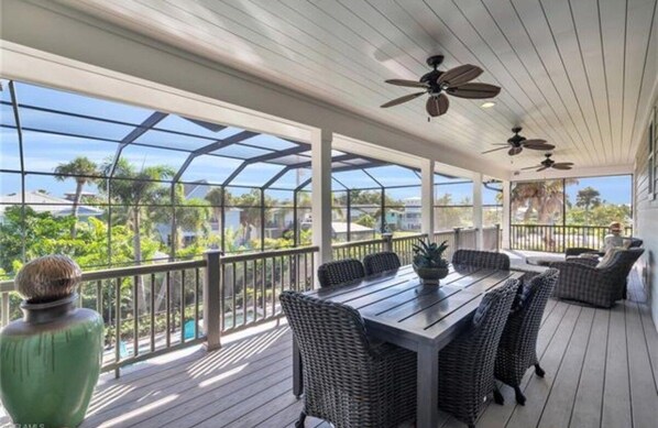A covered outdoor area with a table and chairs, ceiling fans, and a view of the surrounding landscape. - Sunset Breeze (Fort Myers Beach)