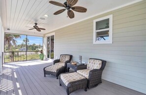 A covered porch with wicker furniture, ceiling fans, and a view of the outdoors.