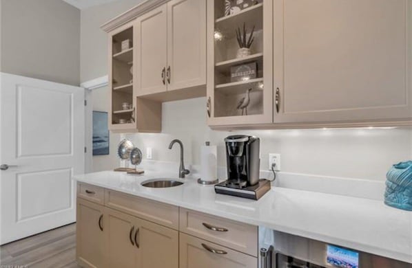 A kitchen with a white countertop, a coffee maker, and a sink.
