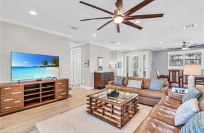 A living room with a television, sofa, coffee table, and ceiling fan. - Sunset Breeze (Fort Myers Beach)