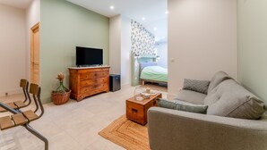 Un salon comprenant un canapé, un téléviseur, une commode en bois et un lit doté d’une tête de lit à motifs.