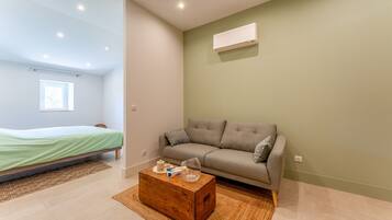 Et moderne værelse med seng, sofa, sofabord i træ og en vægmonteret aircondition.