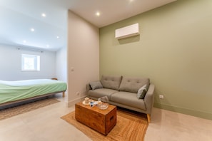 A modern room with a bed, a sofa, a wooden coffee table, and a wall-mounted air conditioner. - Room 'Gérard' with Shared Terrace, Shared Garden, and Air Conditioning (Les Angles)