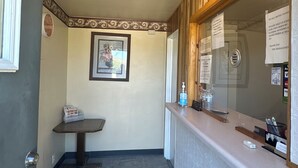 Un hall d’hôtel avec un comptoir d’accueil, un tableau encadré au mur et un panneau d’affichage où sont accrochées des annonces.