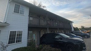 Un immeuble de deux étages doté d’un balcon, d’un parking et de plusieurs voitures garées.