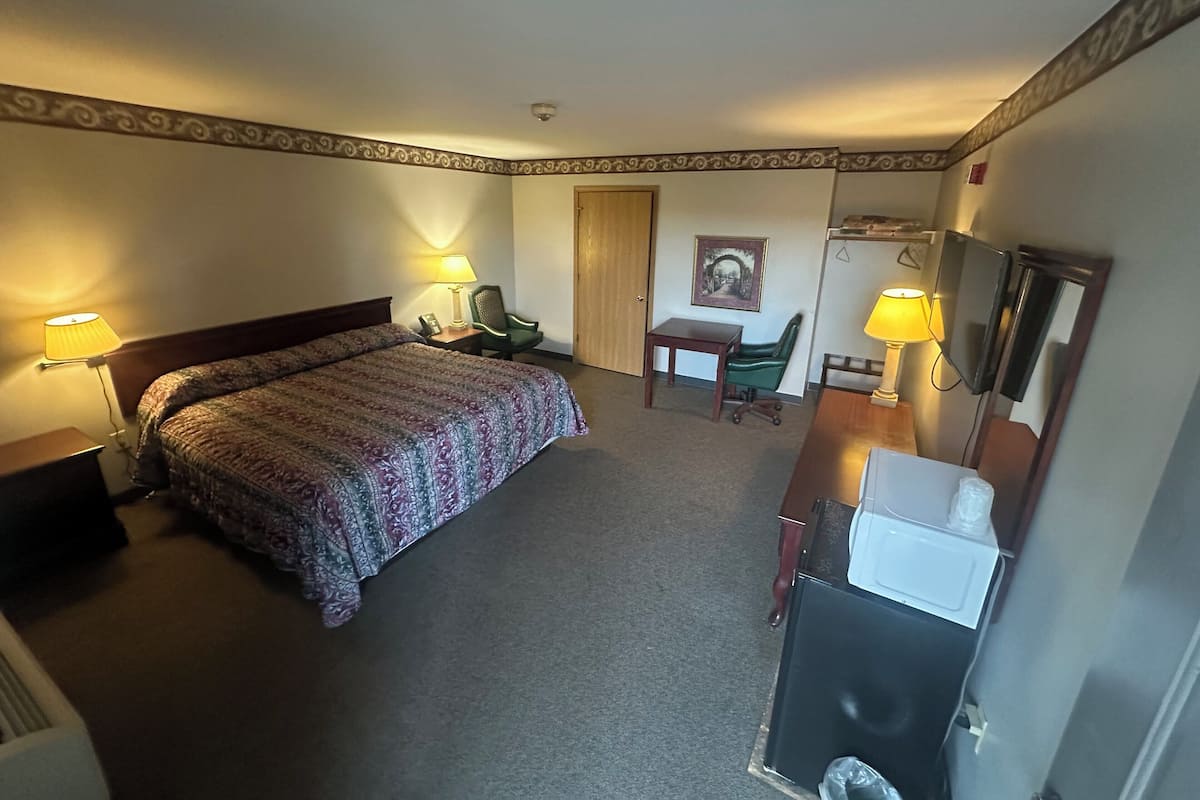 Una habitación de hotel con cama, escritorio, silla, lámpara de escritorio y espejo.
