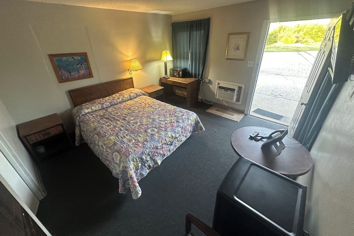 Habitación de hotel con cama, lámparas de noche, escritorio con silla, televisor y ventana con vista a zonas verdes.