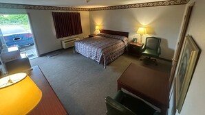 Une chambre d’hôtel avec un lit, deux lampes de chevet, une chaise, un bureau et une voiture garée à l’extérieur.