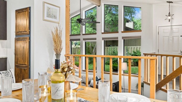 A dining area with a wooden table set for four, a bottle of wine, and candles. Large windows provide a view of greenery outside. - Peaceful Pines | Home Gym & Office, Near Trails (Fort Collins)