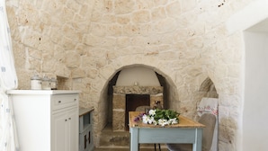Una cocina con paredes de piedra, un horno empotrado, una mesa de madera con flores y un armario blanco con cajones.