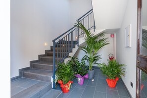 A staircase with a blue railing, potted plants, and a fire exit sign. - 'Blue' Room with Mountain View, Shared Terrace and Air Conditioning (Viagrande)
