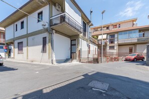 A two-story building with a balcony, a car parked in front, and a stop sign visible. - Room 'Rosa' with Mountain View, Shared Terrace and Air Conditioning (Viagrande)