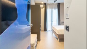 Een hotelkamer met een bed, een bankje, een deur en een raam met gordijnen.