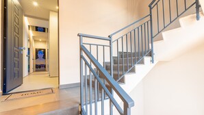 Een moderne trap met metalen leuningen, een deurmat met de tekst 'HOME', en een gang die leidt naar een kamer met een deur.