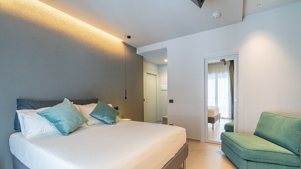 A modern bedroom with a bed, a green sofa, and a bathroom visible through an open door.