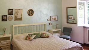 A bedroom with a bed, nightstands, a chair, and wall art. - Villa bifamiliare panoramica in collina con grande giardino (Schignano)