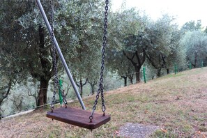 A wooden swing suspended by chains in a park with trees and a grassy area.