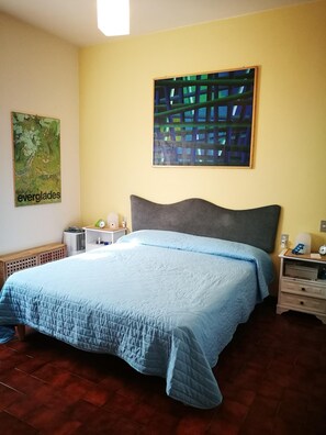 A bedroom with a bed, a nightstand, a wall clock, a framed abstract painting, and a poster on the wall. - Villa bifamiliare panoramica in collina con grande giardino (Schignano)