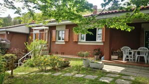 A residential building with a garden area, a patio with chairs, and a small table.