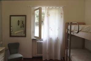Une pièce avec un lit superposé, une chaise, un radiateur, une fenêtre avec un rideau et un miroir accroché au mur.