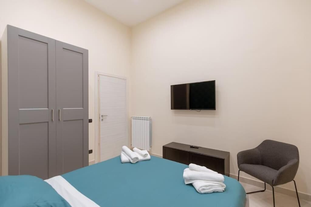 A bedroom with a bed, a grey wardrobe, a television, a radiator, and a grey armchair.