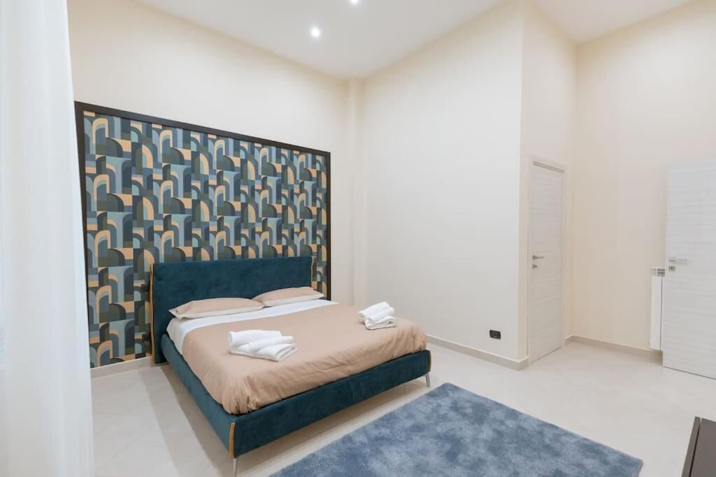 A bedroom with a bed, a patterned headboard, a white door, and a blue rug.
