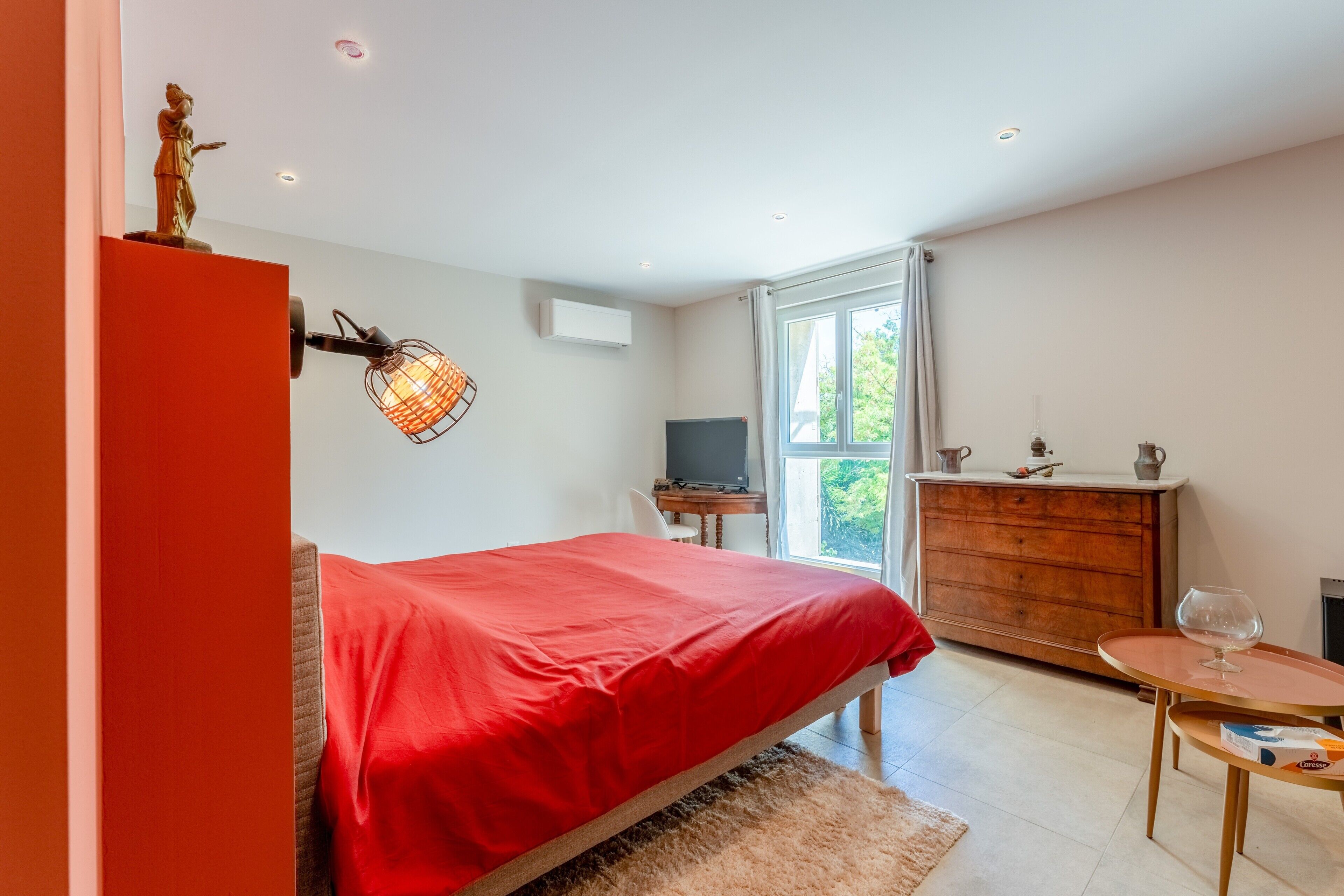 A bedroom with a bed, a dresser, a television, and a window.