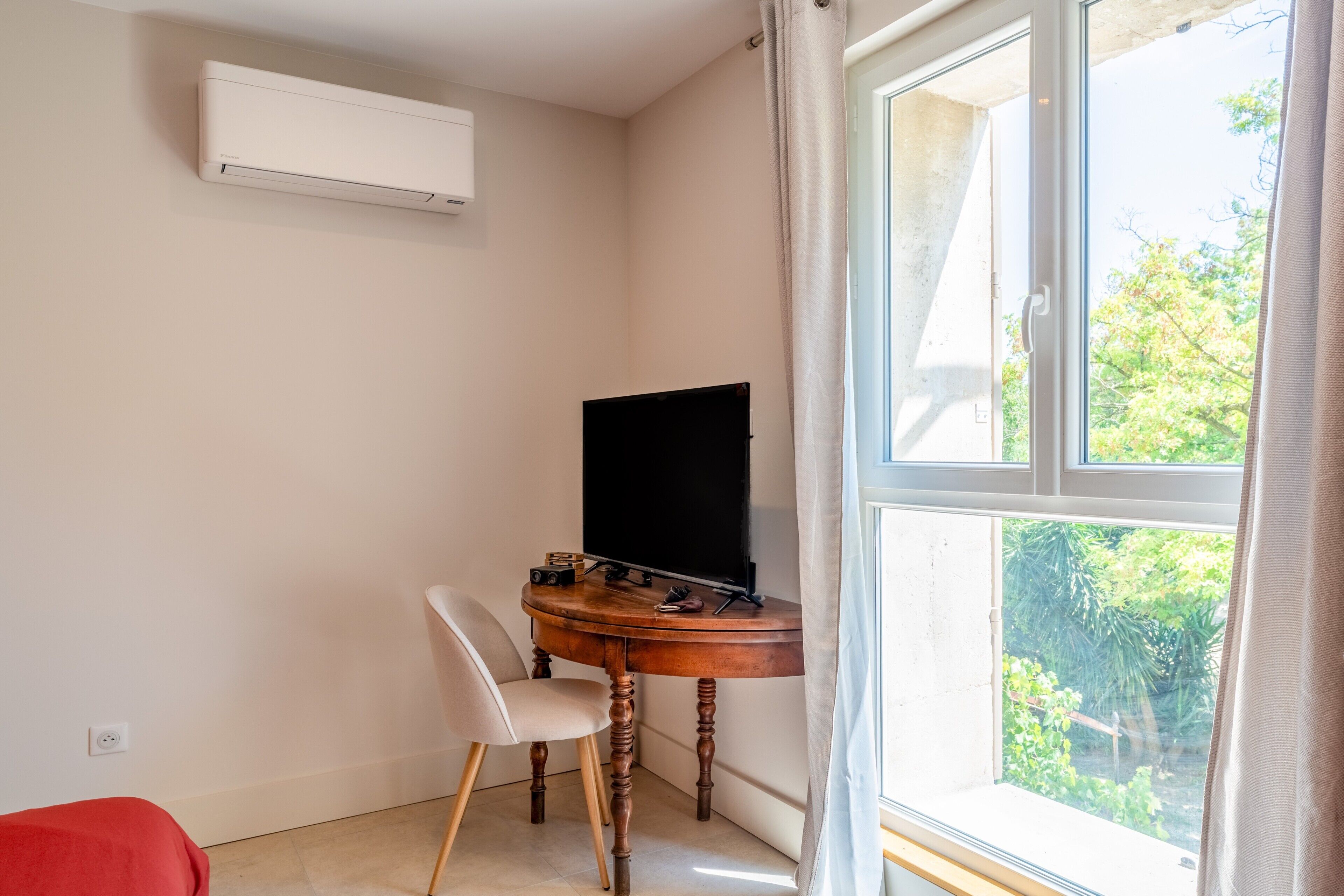Une chambre avec un lit simple, une petite table avec un téléviseur, une chaise et une fenêtre avec des rideaux.