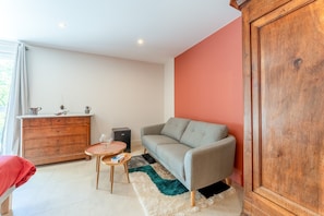 Una sala de estar con sofá gris, aparador de madera, mesa de centro redonda y una silla roja.
