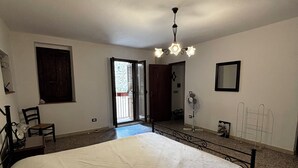 A bedroom with a large bed, a ceiling fan, a window, and a door leading to a balcony. - Stay in the tranquility of Badolato's ancient, atmospheric streets (Badolato)