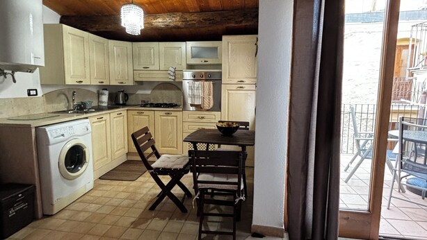 A compact kitchen with wooden cabinets, a washing machine, and a dining area with a table and chairs. - Stay in the tranquility of Badolato's ancient, atmospheric streets (Badolato)