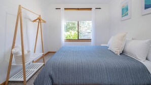 Een slaapkamer met een bed, een houten schommel, een raam en uitzicht op groen.