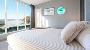 A bedroom with a large bed, a view of the beach, and a circular window.