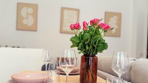 Une table à manger dressée avec des assiettes roses, un vase en verre contenant des fleurs roses et des verres à vin.